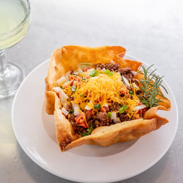 A taco salad in a crispy fried tortilla bowl with ground beef, cheese, tomatoes, and onions.