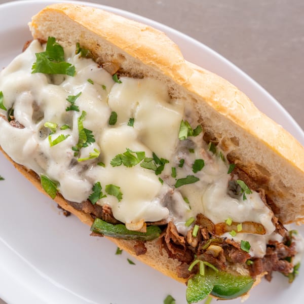 Close-up of a Philly cheesesteak sandwich from Uptown Joes, with melted cheese, steak, and green peppers.