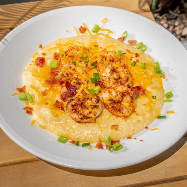 Shrimp and grits with cheese, bacon bits, and green onions on a white plate at Uptown Joes.
