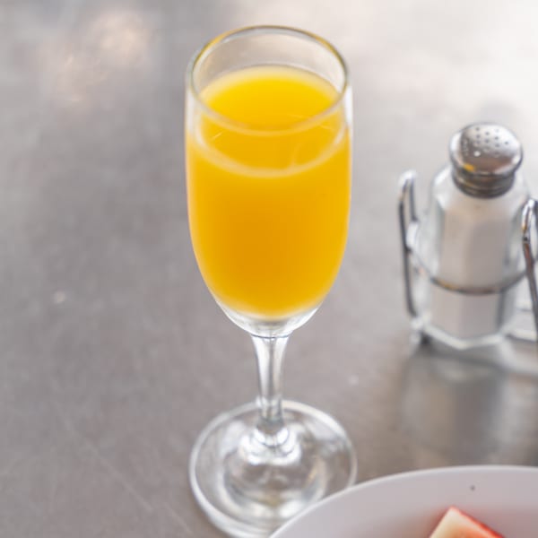 A mimosa in a champagne flute next to a salt shaker and a plate of fruit.