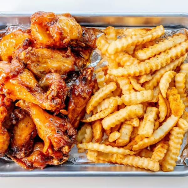 Uptown Joes New York Diner's crispy chicken wings with sauce and crinkle-cut fries on a metal tray.