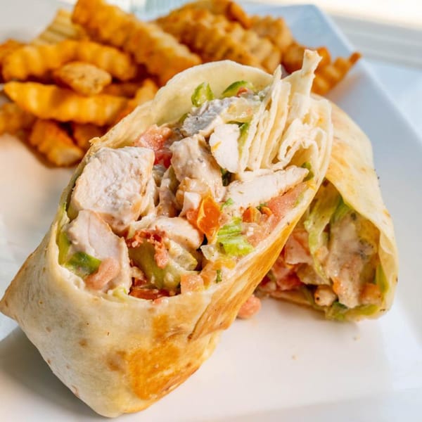 Chicken Caesar wrap, cut in half, with crinkle-cut fries on a white plate at Uptown Joes New York Diner.