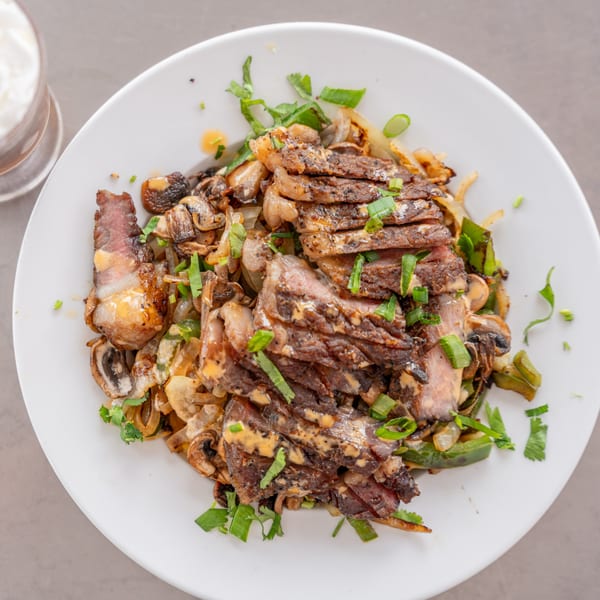Sliced steak with sautéed mushrooms, onions, and green peppers, garnished with fresh herbs.